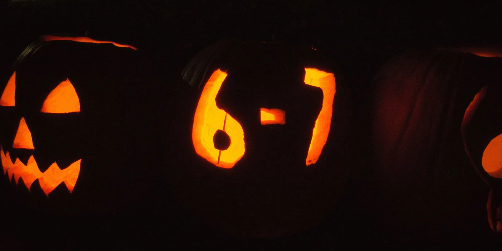 Glowing jack-o'-lanterns at night, the middle one carved with 6-7